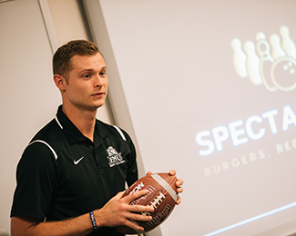 student with a football in front of a classroom