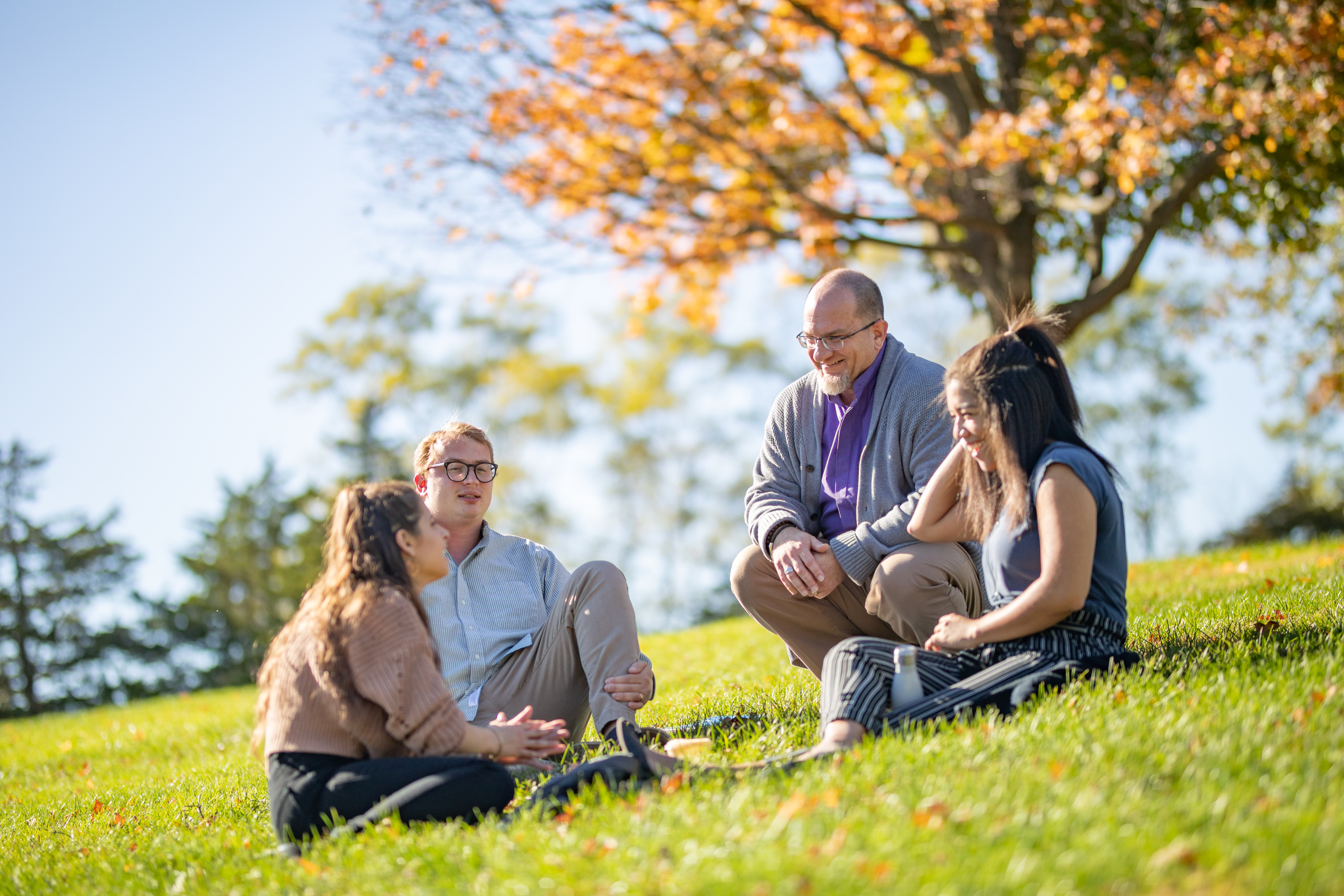 Counseling students outdoors, sitting and chatting in a circle with their professor.